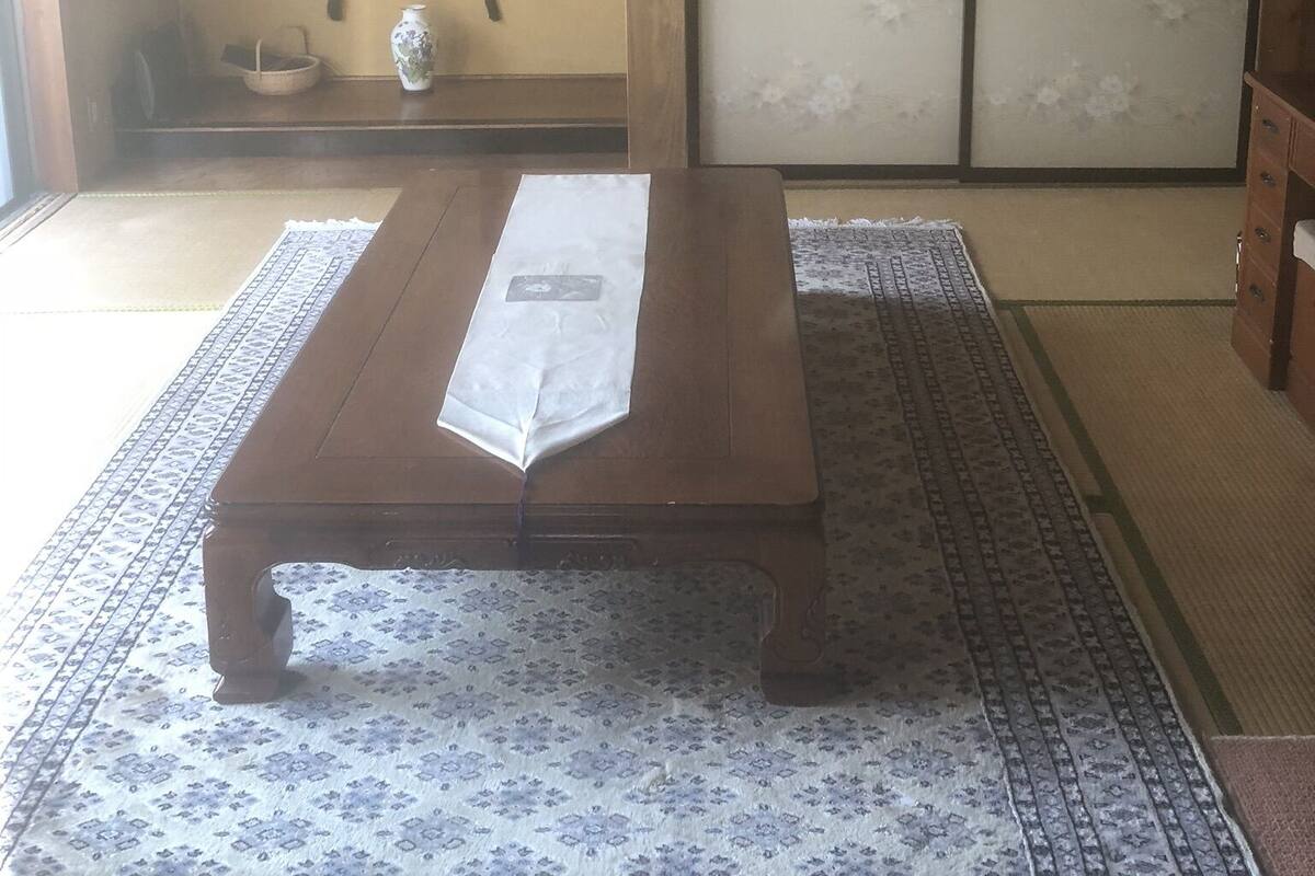 Ein traditioneller japanischer Raum mit Tatami-Böden, einem niedrigen Holztisch, einer Schiebetür und einer aufgehängten Schriftrolle an der Wand.