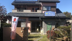 A two-story building with a traditional Japanese architectural style, featuring a tiled roof and a small garden area with potted plants. - Minshuku Tomato House (Tamura)