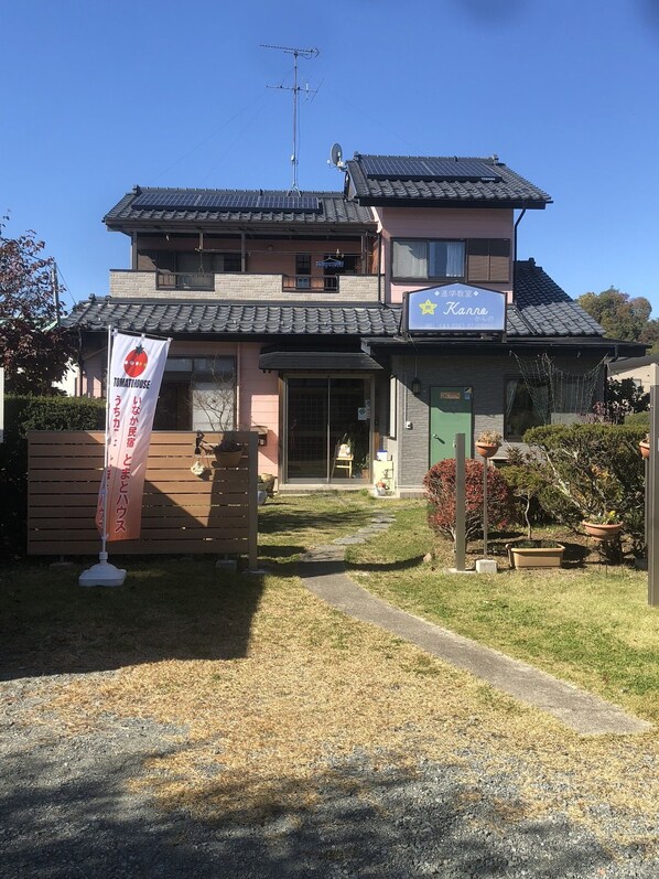 A two-story building with a traditional Japanese architectural style, featuring a tiled roof and a small garden area with potted plants.