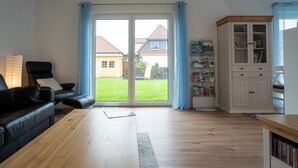 Un salon avec une table basse en bois, un canapé en cuir noir, une bibliothèque et une porte-fenêtre coulissante donnant sur un jardin.