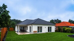 Une maison moderne à deux étages, dotée d’un patio couvert, d’une pelouse bien entretenue et d’une façade en briques.