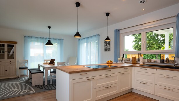 Une cuisine moderne avec des meubles blancs, un plan de travail en bois et des luminaires suspendus.
