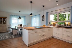 Une cuisine moderne avec des meubles blancs, un plan de travail en bois et des luminaires suspendus.