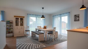 Une cuisine moderne avec un coin repas, comprenant une table en bois, des chaises, un luminaire suspendu et un meuble intégré avec des portes en verre.
