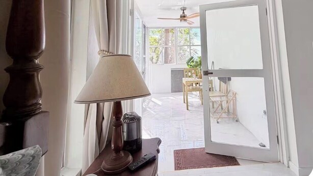 A room with a wooden floor, a lamp, a remote control, and a door leading to an outdoor area with a ceiling fan and a table.