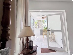 A room with a wooden floor, a lamp, a remote control, and a door leading to an outdoor area with a ceiling fan and a table.