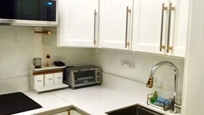 A compact kitchen with white cabinets, a microwave, a toaster, and a sink with a green mat.