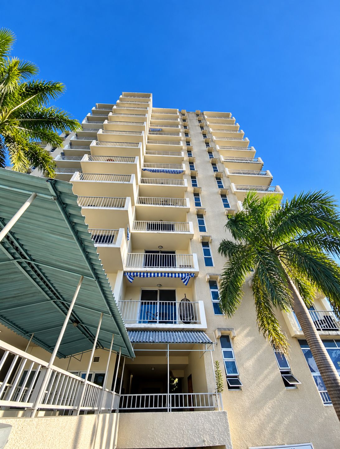 Un hotel de varios pisos con balcones, una entrada cubierta y palmeras.