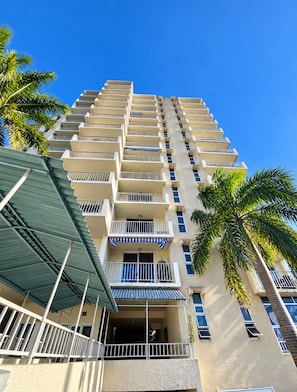 Un hotel de varios pisos con balcones, una entrada cubierta y palmeras.