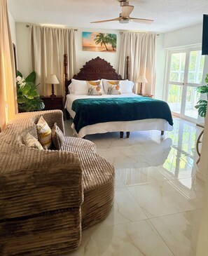 Habitación de hotel con cama, sofá, ventilador de techo y un amplio ventanal.