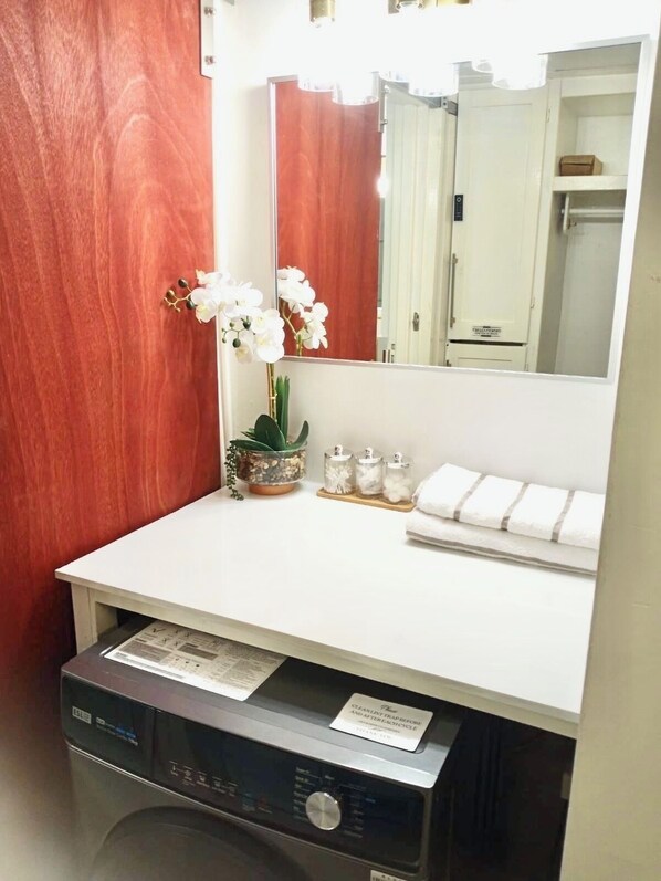 A bathroom with a white countertop, a mirror, a sink, a toilet, and a washing machine.