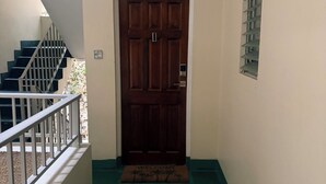A hallway with a wooden door, a staircase to the left, and a window with blinds on the right.