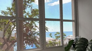 A window with a view of palm trees and a building across the water.
