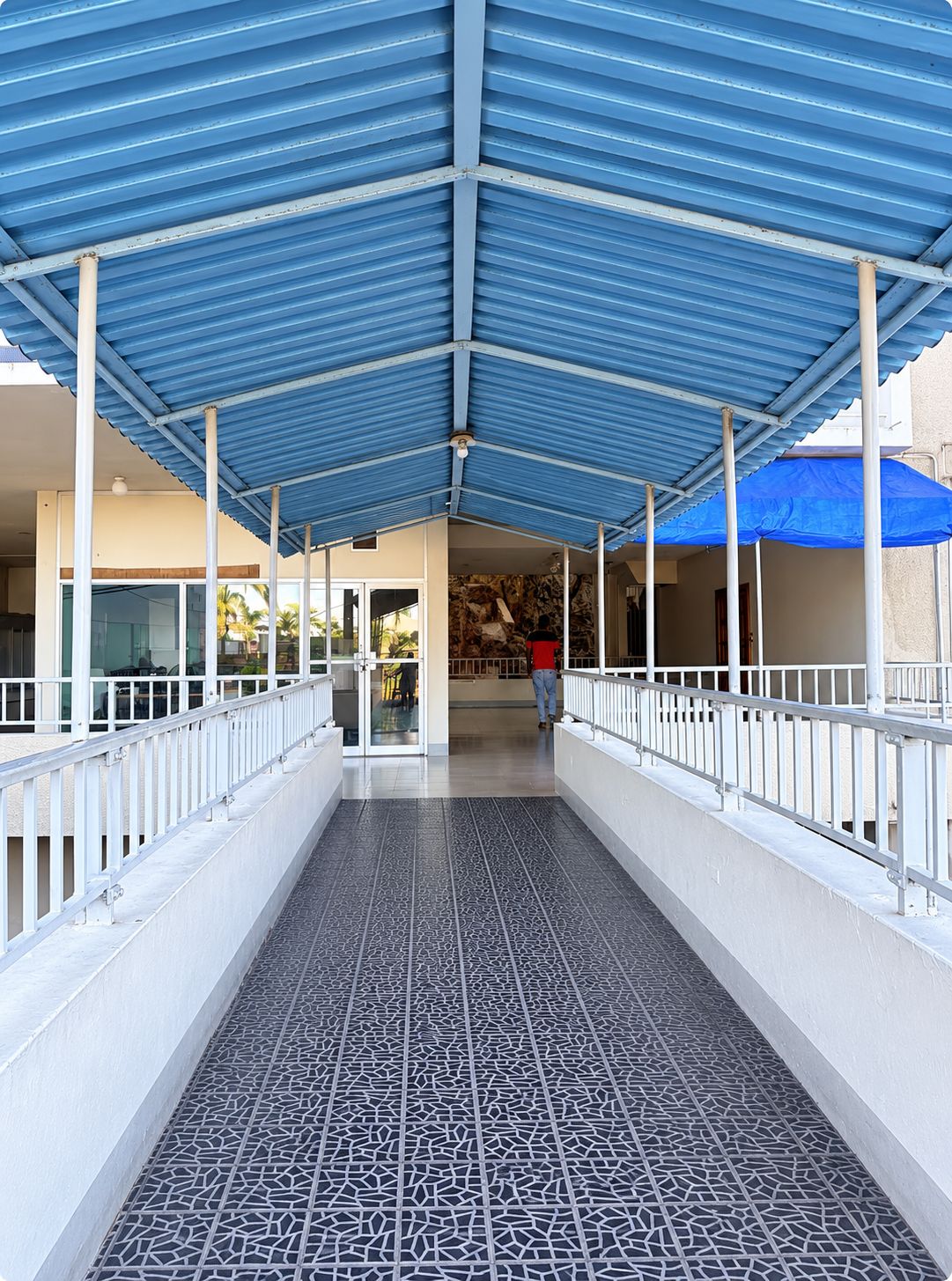 A covered walkway with a patterned floor, white railings, and a blue roof structure.