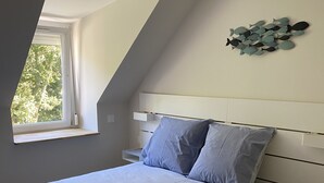 A bedroom with a sloped ceiling, a bed with a patterned bedspread, two pillows, a bedside table, and a wall-mounted decoration. - Newly renovated 80 m2 luxury apartment (Wimereux)