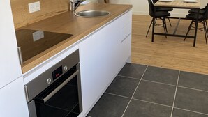 A modern kitchen with a built-in oven, a sink, and a dining area with a table and chairs. - Newly renovated 80 m2 luxury apartment (Wimereux)