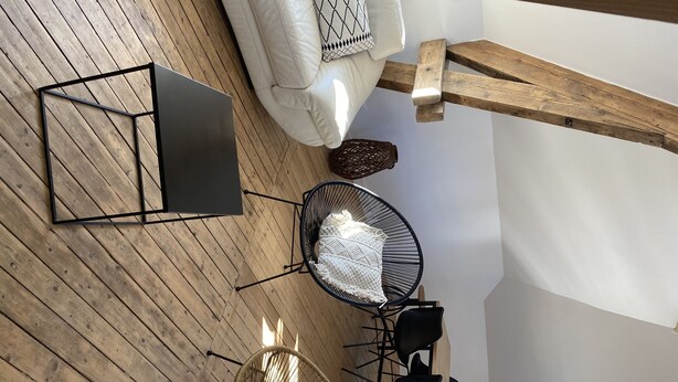 A modern, open-plan living area with a wooden floor, a sofa, a coffee table, a wicker chair, and a dining table with chairs. - Newly renovated 80 m2 luxury apartment (Wimereux)