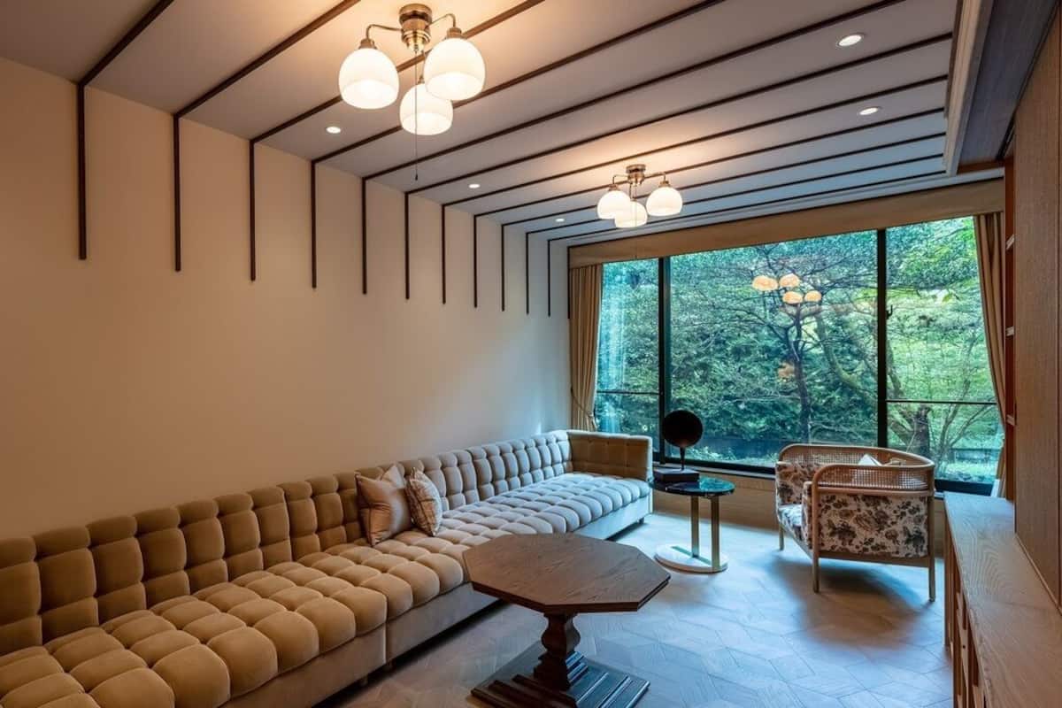 Un salon moderne avec un canapé, une table basse ronde et un fauteuil. De grandes fenêtres offrent une vue sur les arbres.