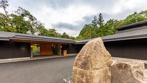 Un bâtiment moderne, avec une grande sculpture en pierre en premier plan, entouré d’un chemin de gravier et d’arbres.