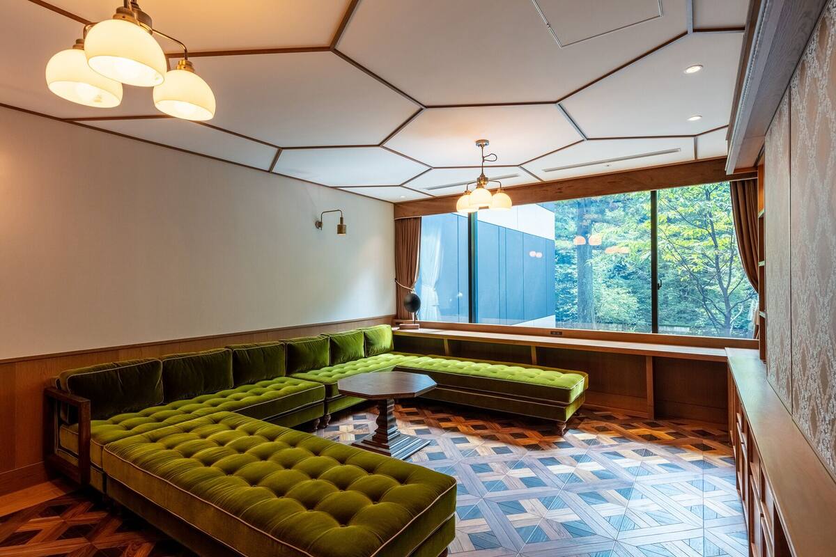 A modern room with a green sectional sofa, a round coffee table, and a large window offering a view of greenery.