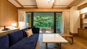 Un salon moderne avec un canapé bleu, une table basse en marbre et une vue sur un jardin luxuriant, visible à travers de grandes portes vitrées.