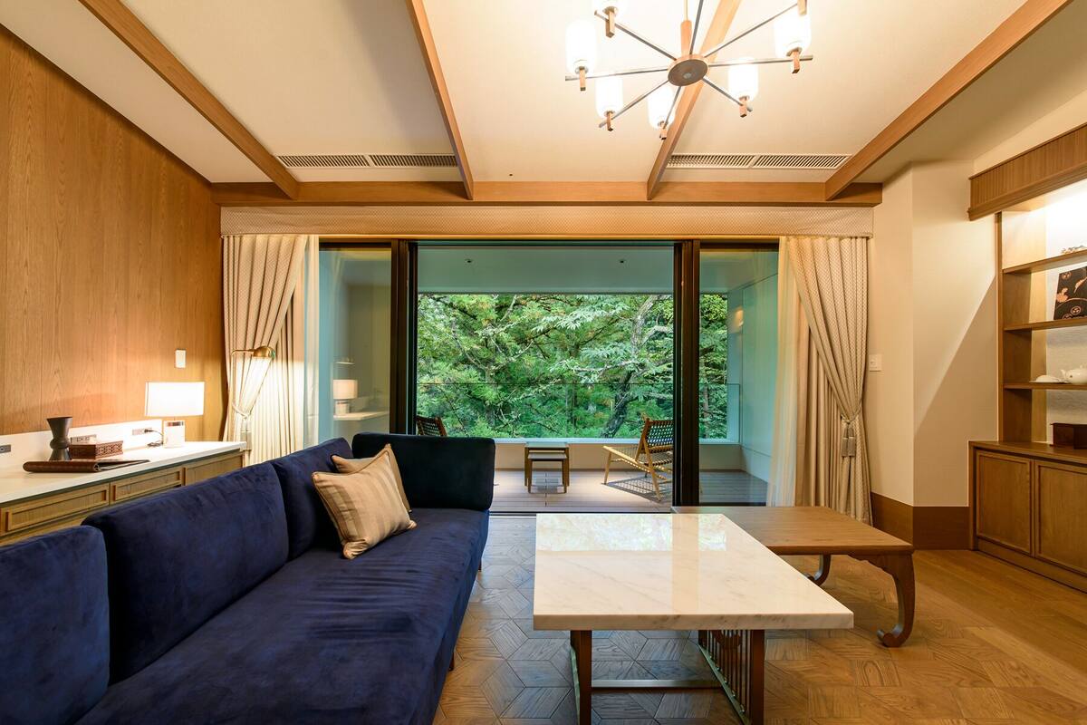 A modern living room with a blue sofa, a marble coffee table, and a view of a lush garden through large glass doors.
