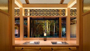 Une pièce avec un bureau en bois, deux chaises, une fenêtre donnant sur des arbres et un paravent décoratif en bois.