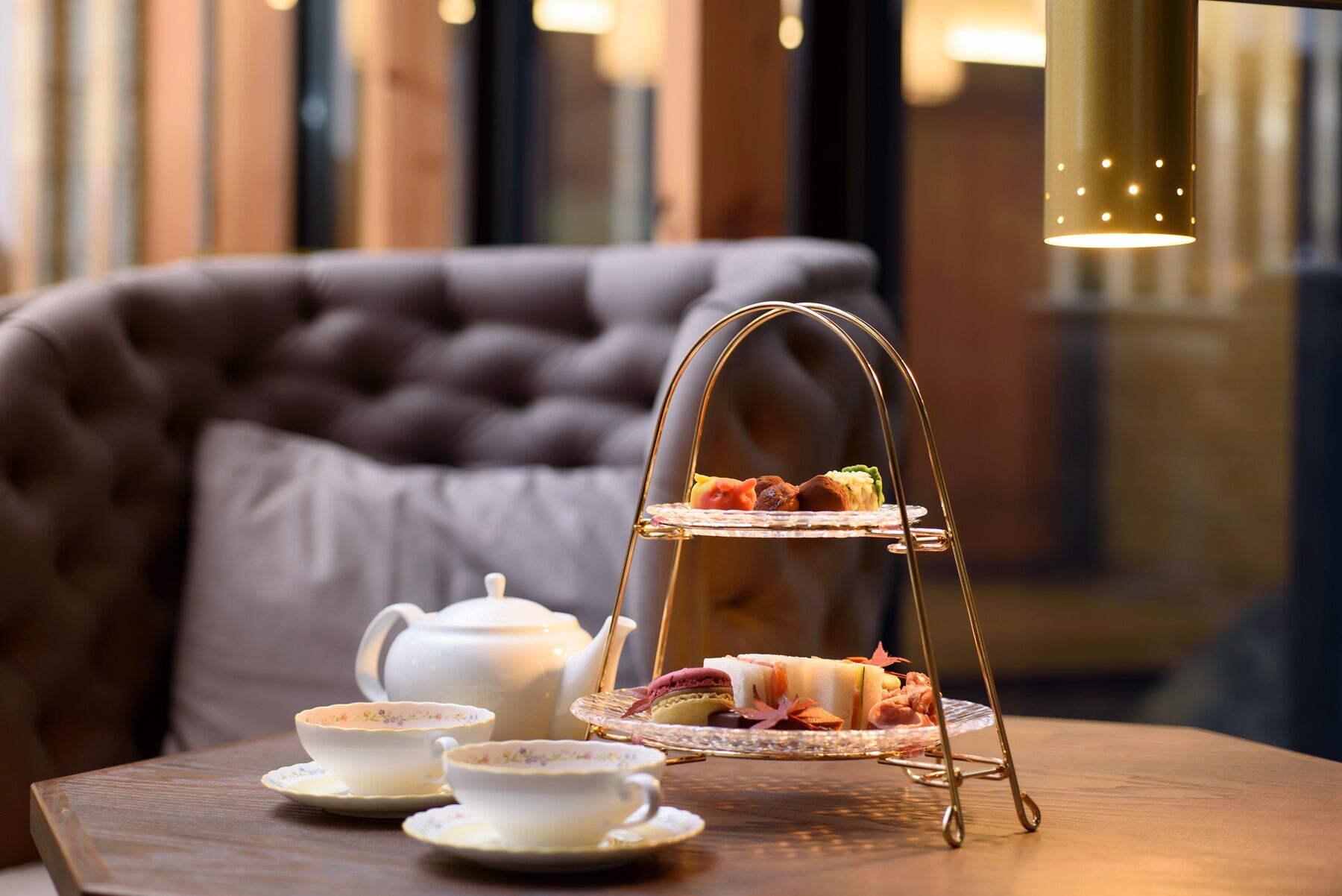 Un expositor de tres niveles con pasteles y macarons sobre una mesa de madera, acompañado de tazas de té y una tetera.