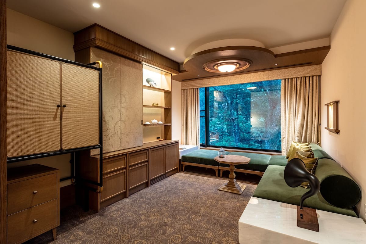A room with a large window, a green sofa, a wooden cabinet, and a patterned carpet.
