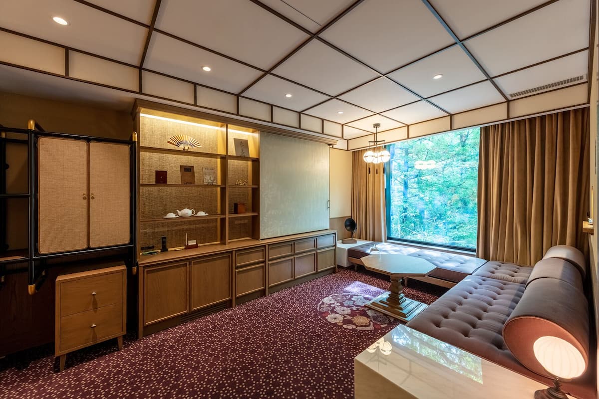 A traditional Japanese-style room with tatami flooring, a low wooden desk, a cushioned seating area, and a large window with a view of greenery.