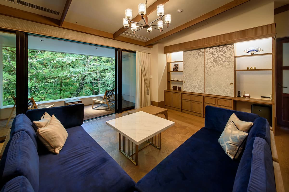 A modern living room with a large window, a sofa set, a coffee table, and a traditional Japanese-style cabinet.