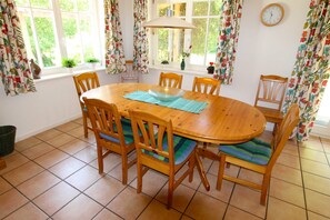 A dining area with a wooden table and chairs, a window with curtains, and a clock on the wall.