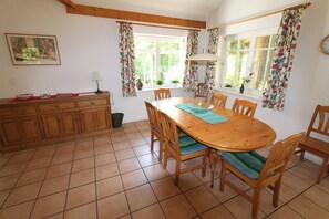 Un coin repas avec une table et des chaises en bois, une fenêtre avec des rideaux, un buffet rempli de vaisselle et une horloge au mur.