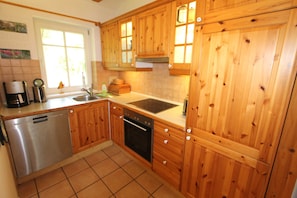 Una cocina con armarios de madera, lavavajillas, pileta y ventana con luz natural.