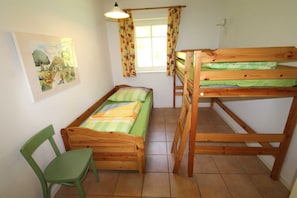 Una habitación con una cama litera, una cama individual, una silla y un ventanal con cortinas.