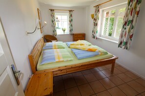 A bedroom with a wooden bed, a nightstand, a chair, a dresser, and a window with curtains.
