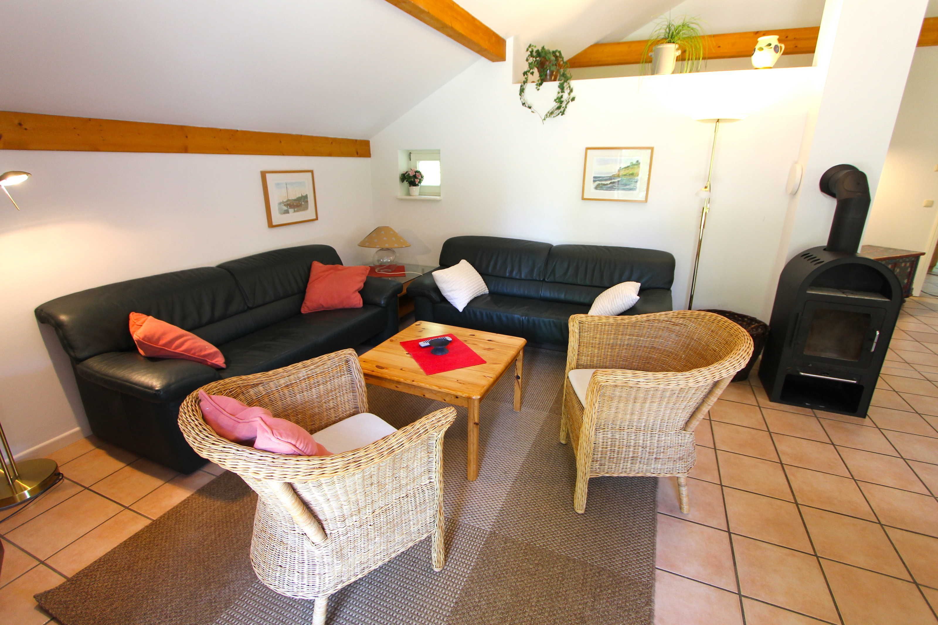 Ein Wohnzimmer mit einer schwarzen Ledersofa, zwei Korbstühlen, einem Holztisch und einem Kaminofen.