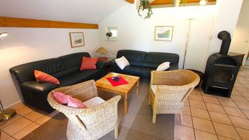 Ein Wohnzimmer mit einer schwarzen Ledersofa, zwei Korbstühlen, einem Holztisch und einem Kaminofen.