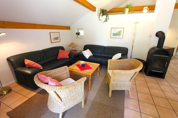 Una sala de estar con un sofá de cuero negro, dos sillones de mimbre, una mesa de centro de madera y un estufa de leña.