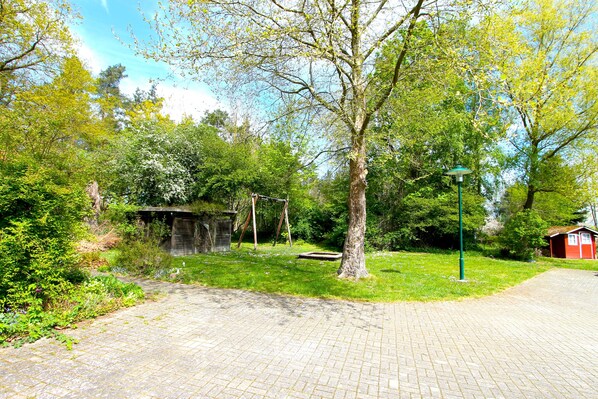 A paved pathway leading to a rustic wooden structure surrounded by lush greenery and trees.