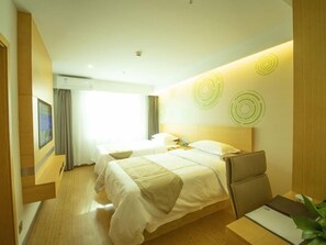 Ein Hotelzimmer mit einem großen Bett, einem Schreibtisch und einem Stuhl. Es gibt ein Fenster mit Vorhängen, eine Wand-Klimaanlage und eine Wand mit kreisförmigen Mustern.