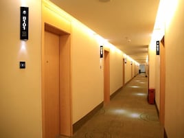 Un pasillo de hotel con puertas numeradas, suelo alfombrado y un cubo de basura.