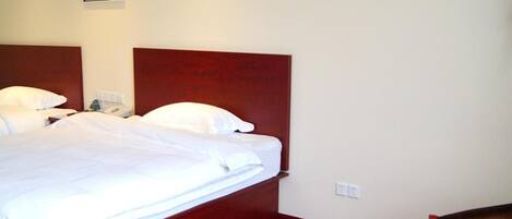 A hotel room with a large bed, a wooden headboard, a bedside table with a phone, and a small round table with toiletries.