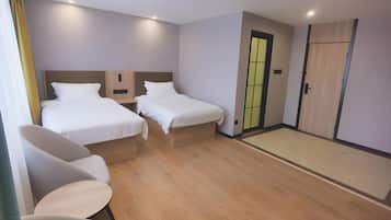 Habitación de hotel con dos camas individuales, una zona de estar pequeña con una mesa, y una puerta corredera que da a un armario.