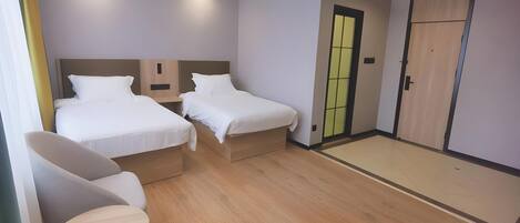 A hotel room with two single beds, a small seating area with a table, and a sliding door leading to a closet.