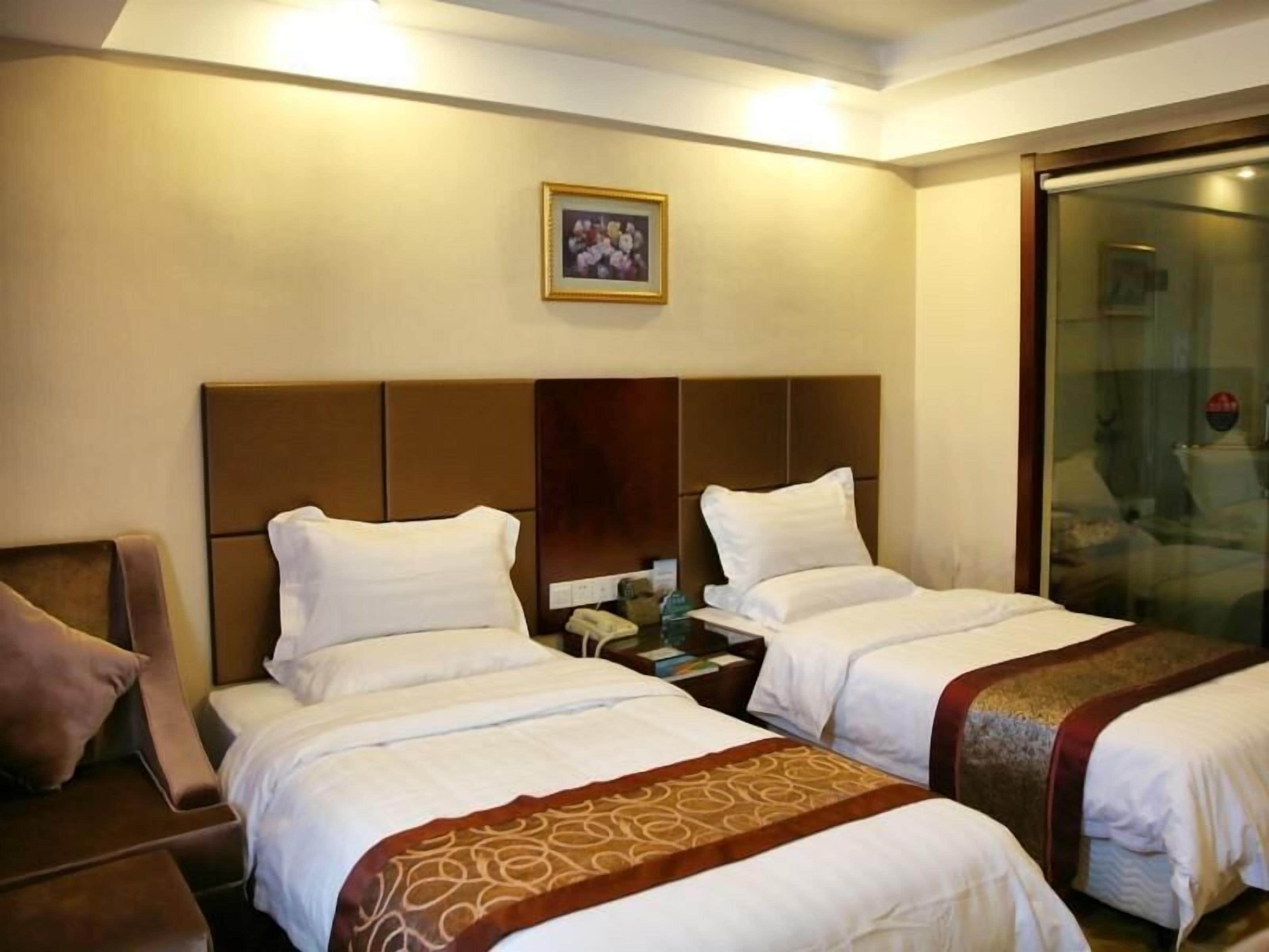 A hotel room with two beds, a wooden headboard, a nightstand, a chair, and a glass door leading to a bathroom.