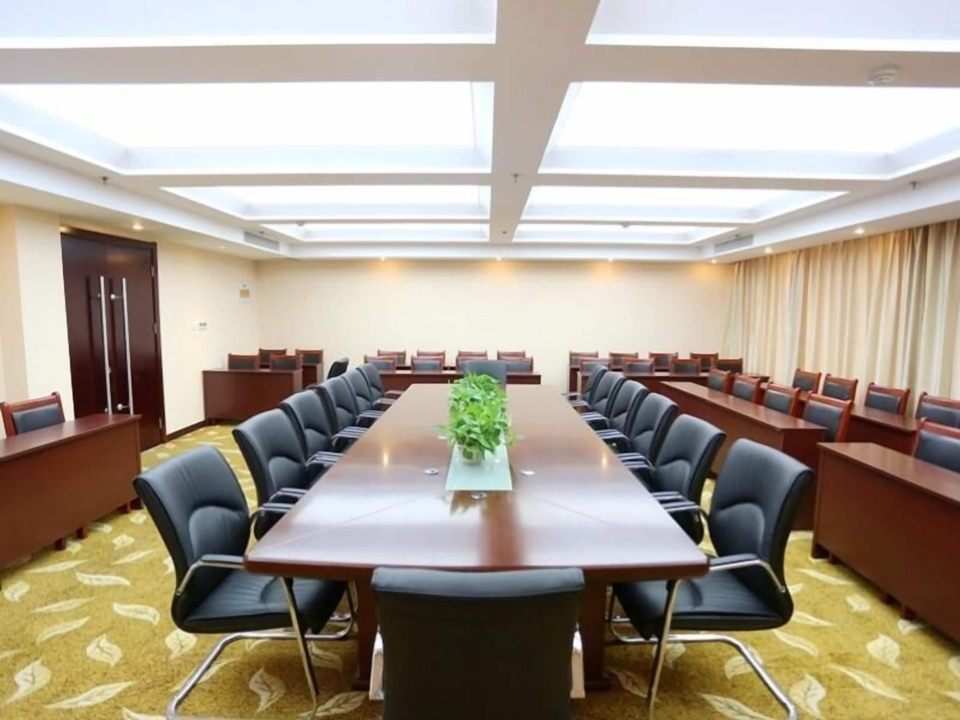 A conference room with a long table, multiple chairs, a potted plant, and a high ceiling with skylights.