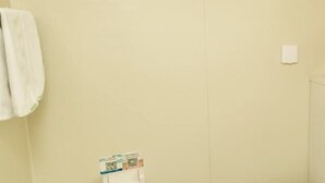 A plain wall with a white towel hanging on the left and a small item on the floor.