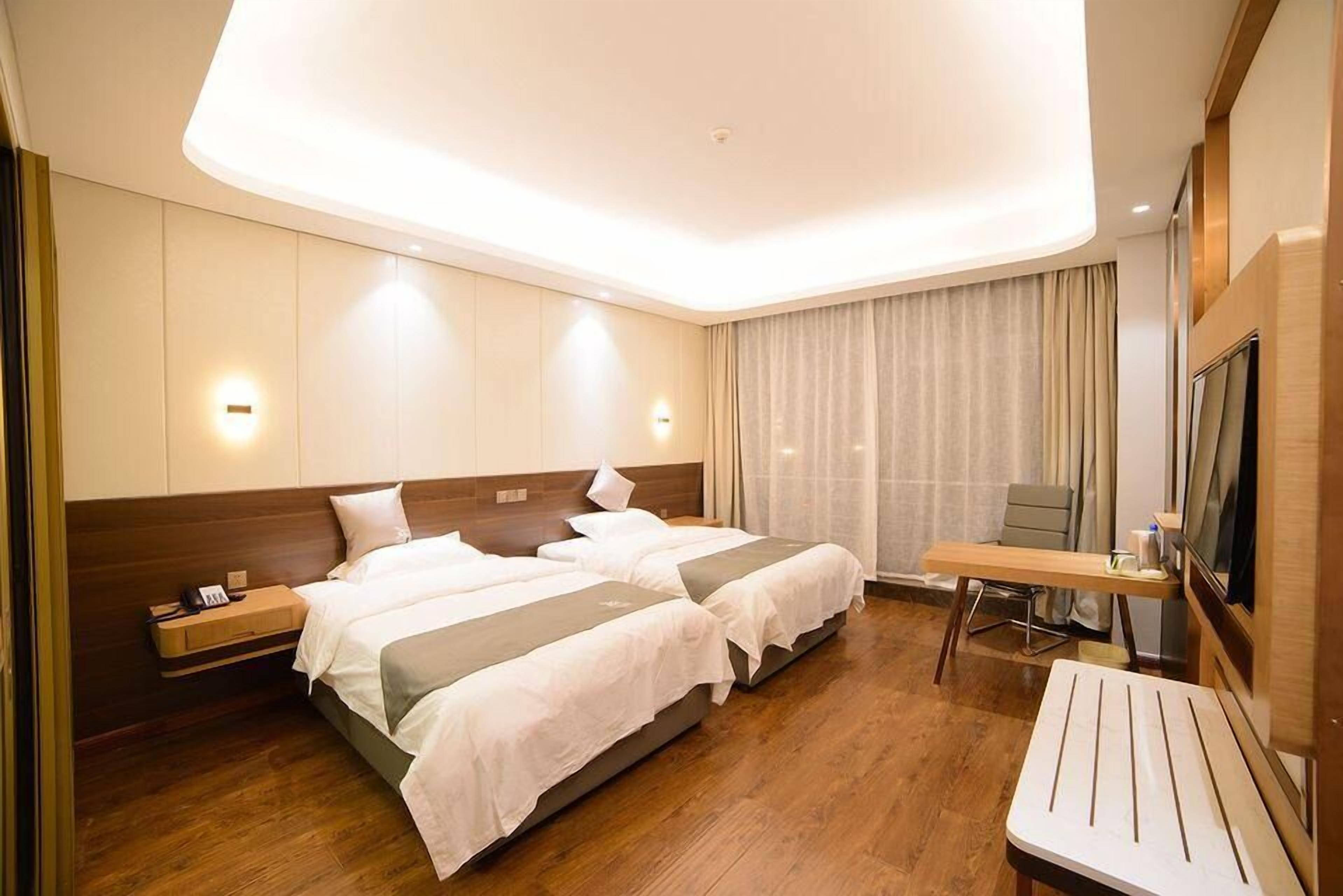 A hotel room with two beds, a desk, and a TV.