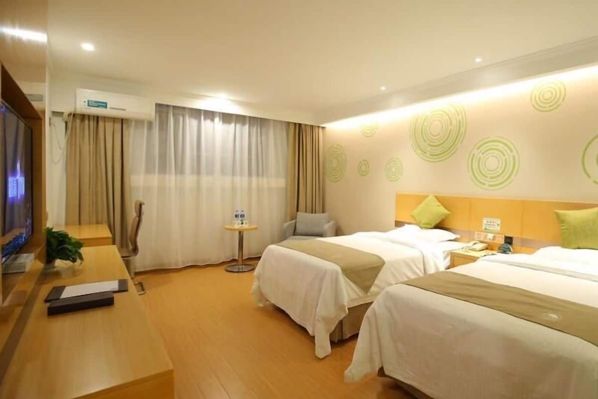 Una habitación de hotel con dos camas, un escritorio, un televisor y una mesita con una planta.